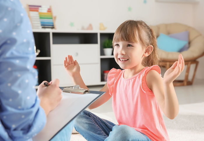 A child holds her hands apart while an adult in the foreground writes something down